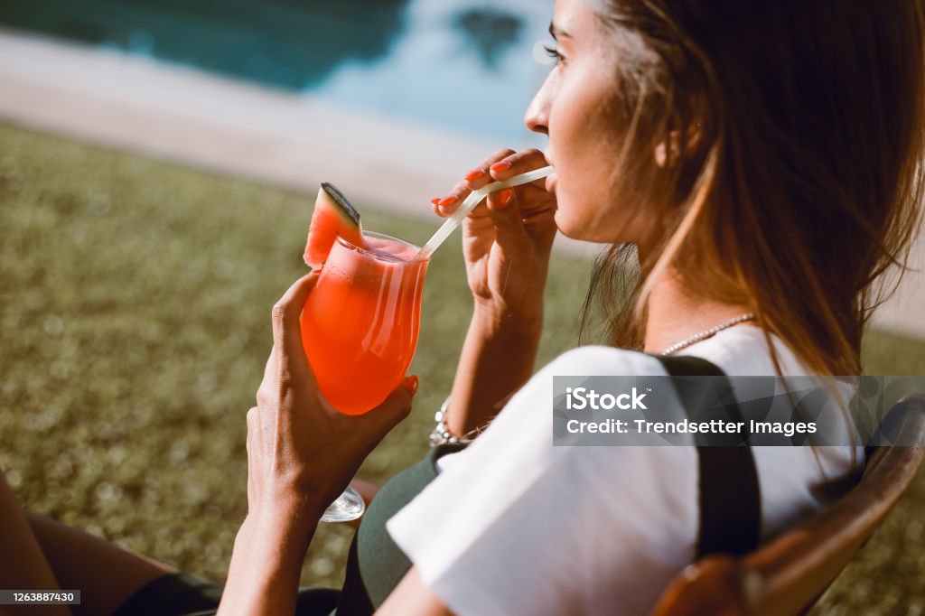 Beautiful woman drinking cocktail near the pool Beautiful woman drinking cocktail near the pool - Spring and Summer Adult Stock Photo