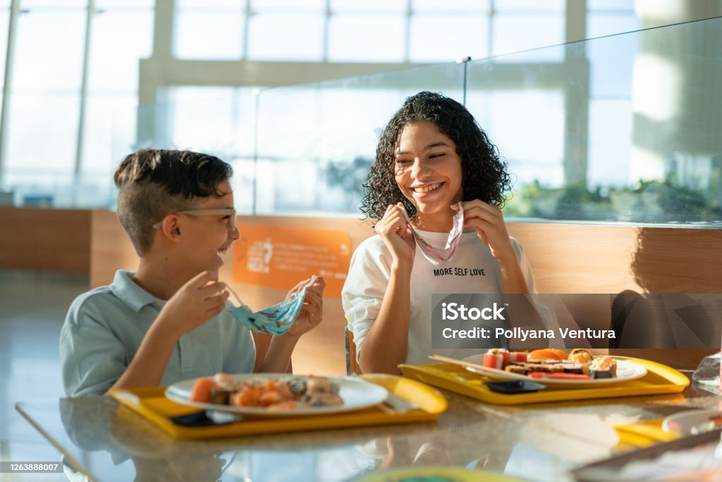 People living the new normal in the coronavirus pandemic Siblings, Smiling, Removing, Protective mask, Lunch Child Stock Photo