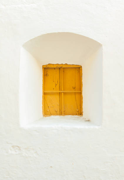 an old yellow wooden window in a white adobe wall. Outdoors. Spain.