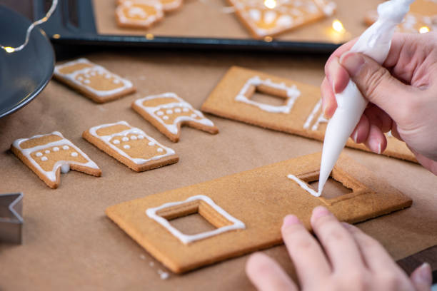 Young woman is decorating Christmas Gingerbread House cookies biscuit at home with frosting topping in icing bag, close up, lifestyle. Young woman is decorating Christmas Gingerbread House cookies biscuit at home with frosting topping in icing bag, close up, lifestyle. decorating a cake photos stock pictures, royalty-free photos & images