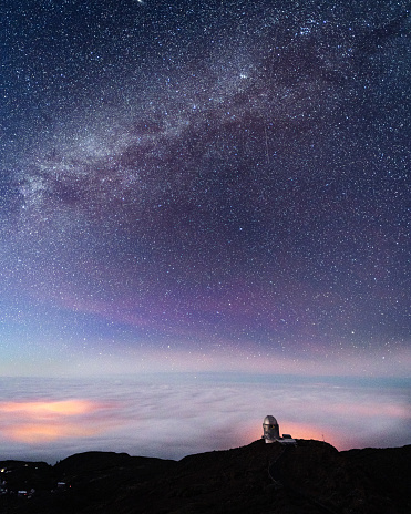 Starry sky with Milky Way over cloud covered valley and astronomical observatory on edge of mountain