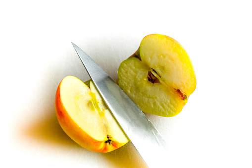 A Katy apple cut in half on a kitchen chopping board.