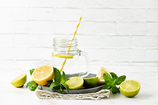 Shot of Mint lemonade with slices of lemons and mint leaves against white brick wall.