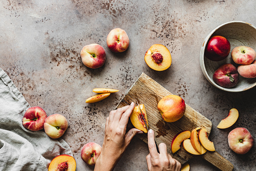 Hands of a woman cutting fruits on chopping board. Female making slices of a fresh peaches on kitchen counter.