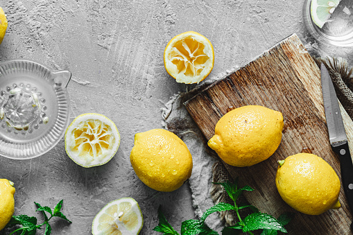 Top view of a lemons on cutting board with mint leaves and juicer on white background.