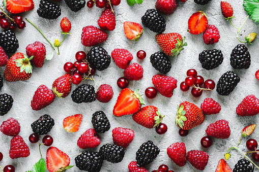 Top view of variety of tropical fruits flay lay on white background. Directly above shot of a blackberries, raspberries, strawberries, plums, peaches, apricots and apples.