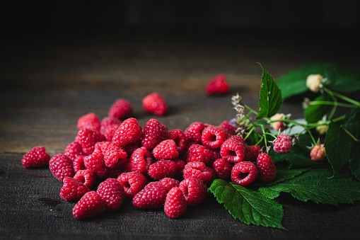 Freshly picked raspberries with leaves on a wooden table. Heap of red fresh raspberries.