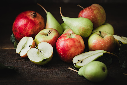 Shot of apples, pears and pomegranate on a wooden table. Close-up of half cut and full fruits.