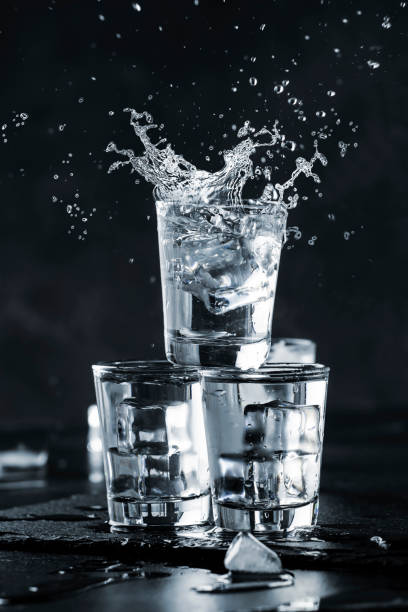 vodka splash with spray from shot glasses on black stone background, iced strong drink in misted glass - russian shot imagens e fotografias de stock