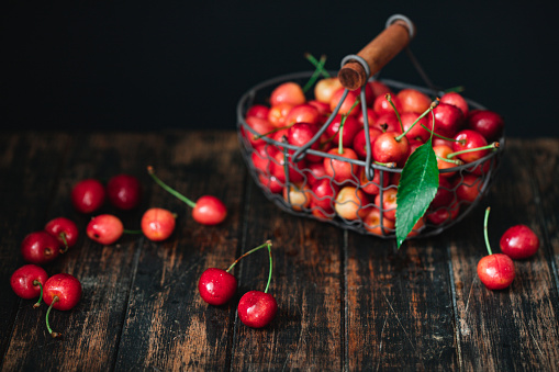 Bunch of ripe cherries with peduncles in a basket. Large collection of fresh red cherries on wooden table.
