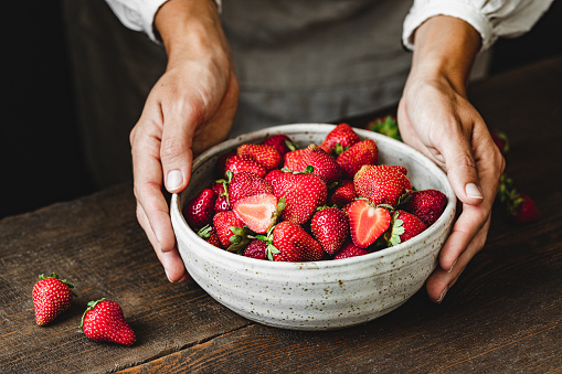 Woman holding a bowl of fresh berries. Ripe strawberries in a ceramic bowl over wooden table.