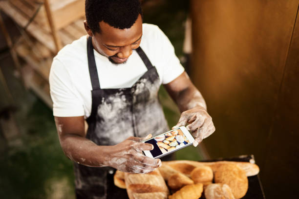 Cropped shot of a male baker taking a picture on his cellphone of a selection of freshly baked bread