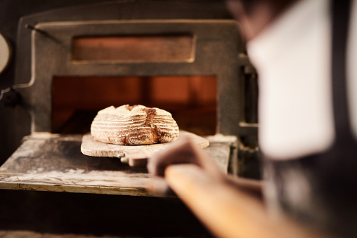 Cropped shot of a male baker removing freshly baked bread from the oven