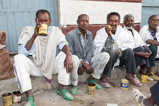 Hamd Ela, Ethiopia, February 23 2015: Ethiopian men sit outside in the street talking and drinking a local drink from old tin cans