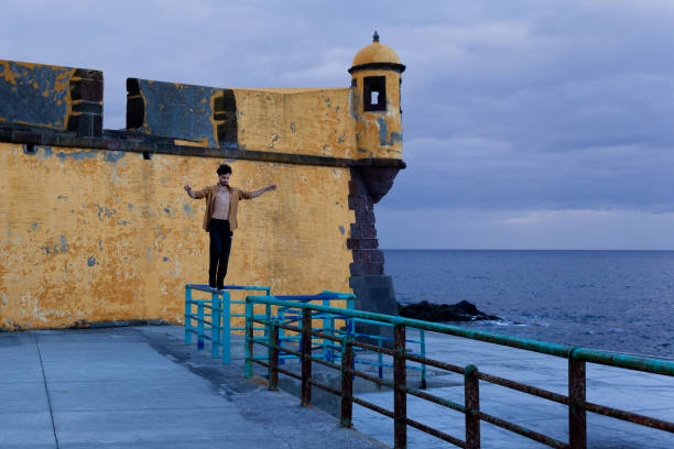 Young man standing on the railing near São Tiago fort in Funchal during sunrise