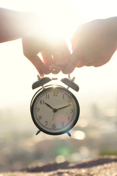 istock two hand holding alarm clock sunset outdoor. Best friends 1263896310
