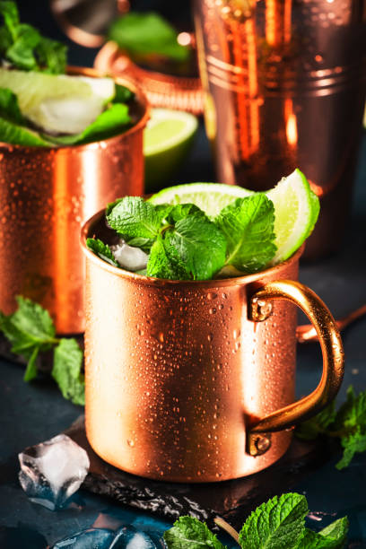 istock Moscow mule cocktail in copper mug with lime, ginger beer, vodka and mint. Blue table, copper bar tools, copy space 1263897095