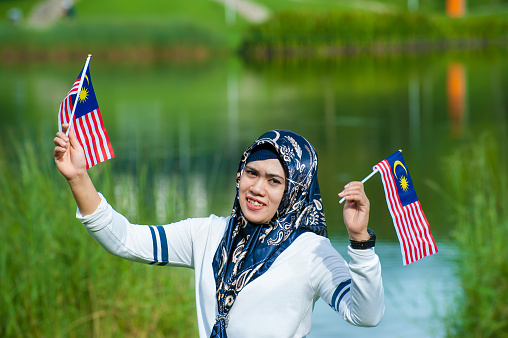 Two Malaysian women with hijab waving Malaysian flags with pride. High Independence Day Spirit and Patriotic Concepts