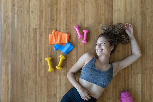Portrait of a healthy woman with sports equipment around her after working out at home - fitness concepts