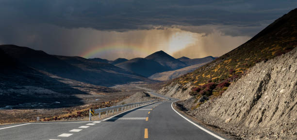 Driving travel on an empty asphalt road through the countryside fields towards the setting, scenic road at Yading China. Beautiful panorama landscape, cloudy black sky storm rain background.
