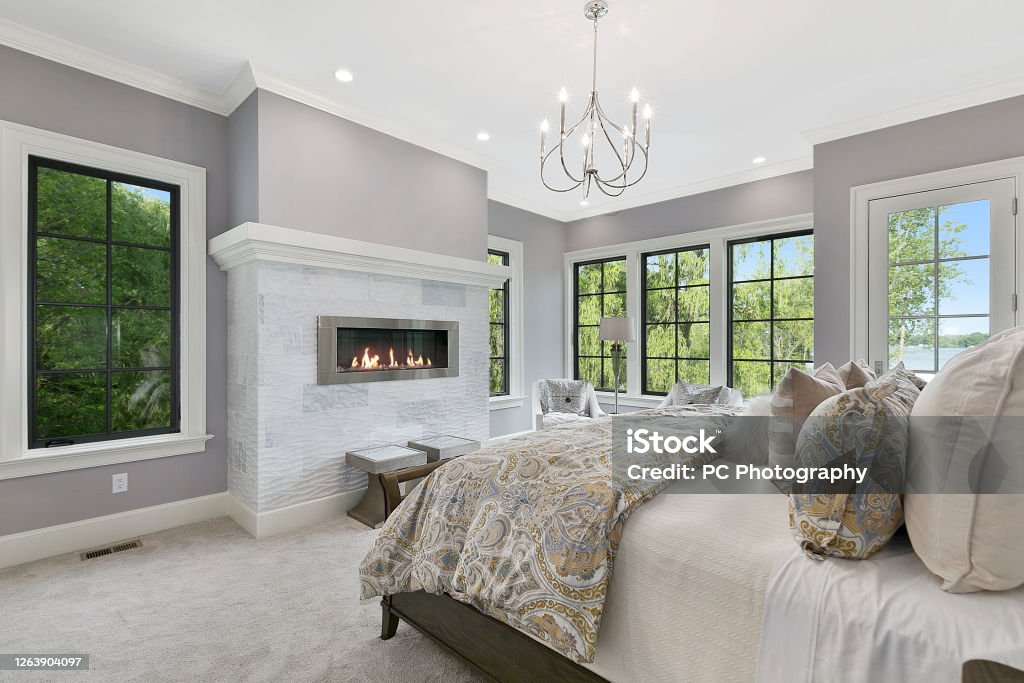 Gorgeous bedroom with large stately fireplace for romantic evenings Simple chandelier and many comfortable options for lovely night at home Bedroom Stock Photo