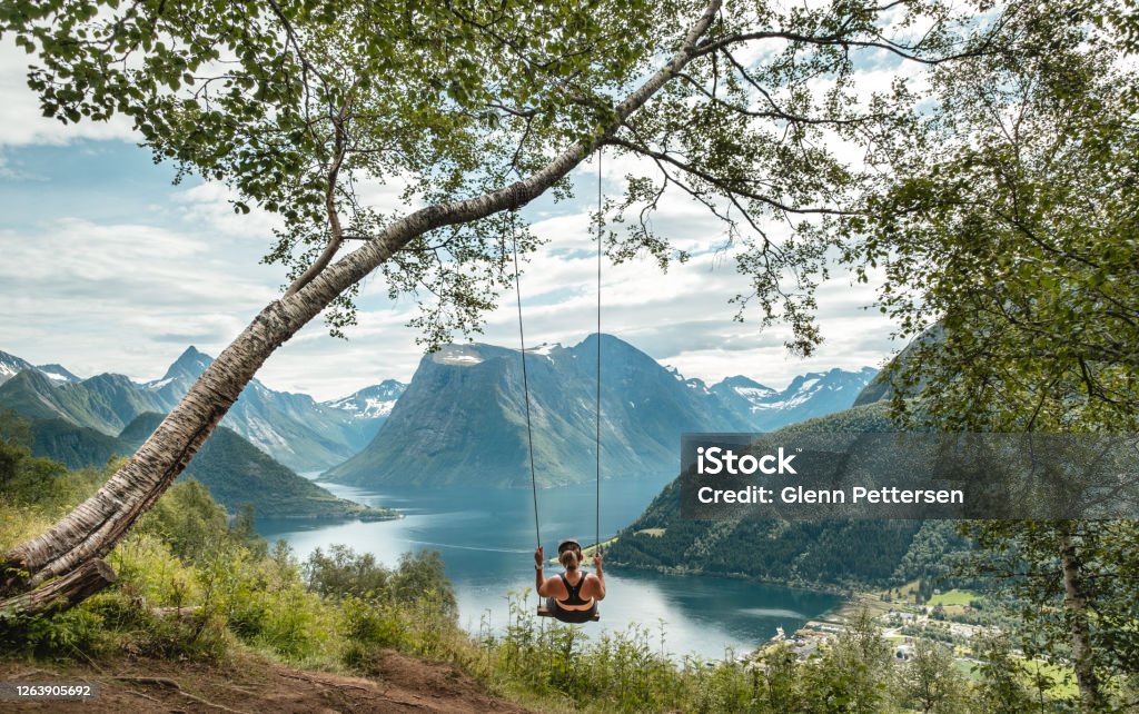 Woman swinging into nature in Norway. Young woman swinging into fjord and mountains in Sunnmore, Norway. Norway Stock Photo