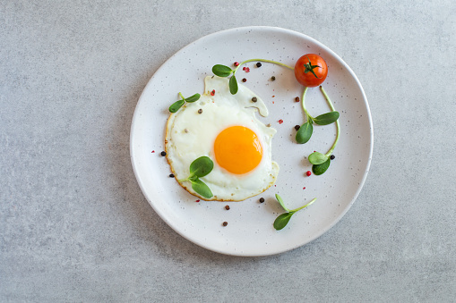 Fried scrambled egg with greens and tomato in white plate on grey background
