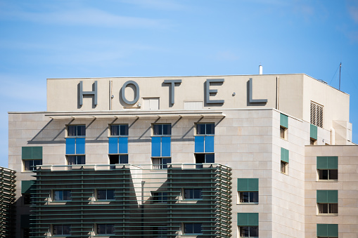 Close-up view on blue clear sky background of the building exterior facade of a simple and common hotel with the letters HOTEL in front. Taken on Saone riverbank in summer, near Lyon city in France, Auvergne-Rhone-Alpes region, in Europe.