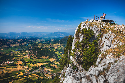 Couple of tourists, a man and a woman, enjoy a viewpoint over french landscape. This photo was taken during a sunny summer day at the top of La Dent Du Chat mountain peak in end of Bugey mountains, in border of Ain and Savoie department, in Auvergne-Rhone-Alpes region in France, Europe.