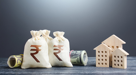 Indian rupee money bags and residential buildings figures. Investments in real estate. Mortgage loan. Financing the construction and renovation of housing. Municipal budget management. Taxes.
