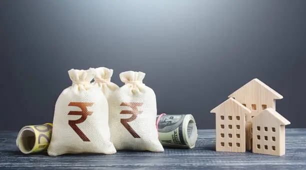 Photo of Indian rupee money bags and residential buildings figures. Investments in real estate. Mortgage loan. Financing the construction and renovation of housing. Municipal budget management. Taxes.