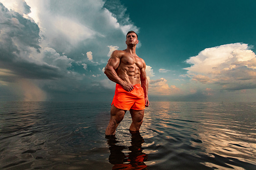 Fit athlete bodybuilder on the beach. Attractive young man lifeguard on a tropical seashore. A thunderstorm is behind the man