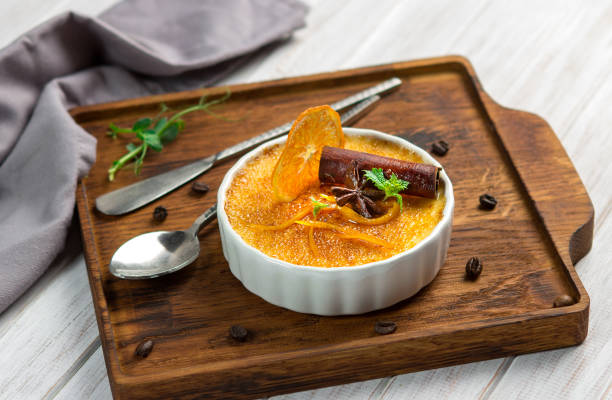 baked orange creme brulee dessert in white bowl with cinnamon and mint on wooden background - dessert ready to eat creme brulee food imagens e fotografias de stock