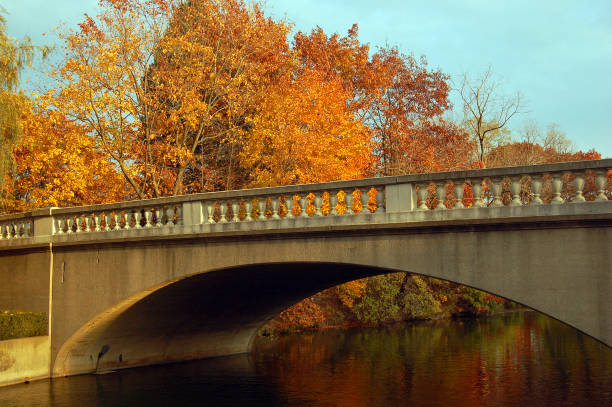 A stone bridge spans a tranquil lake in Mounds Cemetery in Racine, Wisconsin during autumn