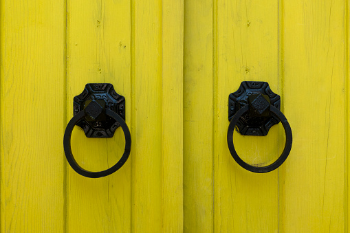 Old door knocker on neon yellow colored wooden door
