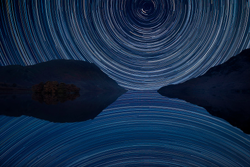 Digital composite image of star trails around Polaris with Beautiful Winter Crummock Water landscape in Lake District England
