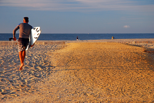 Ocean City, NJ, USA August 24, 2013 An adult man makes his way to the ocean for early morning surfing at Ocean City, New Jersey