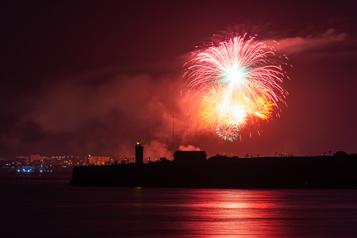 Festive salute over the city of Sevastopol on the day of the Navy. Bright multicolored flashes of fireworks. The concept of the celebration. Night shooting of the city. Silhouette of the lighthouse.