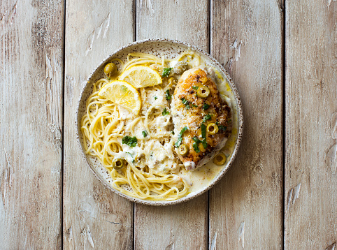 Spaghetti with creamy lemon sauce, parmesan cheese  and fried chicken breast on natural wooden table. Flat lay
