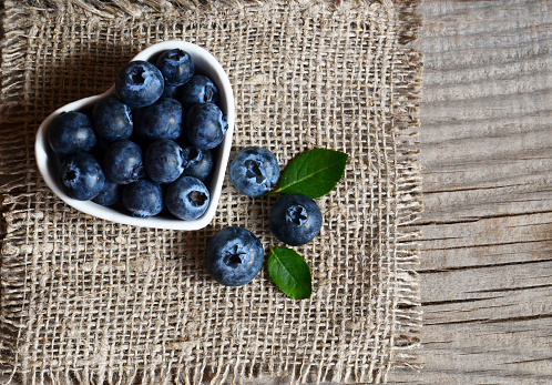 Freshly picked organic blueberries in a white heart shaped bowl on old wooden background.Blueberry. Bilberries.Healthy eating,vegan food or diet concept with copy space.Selective focus.