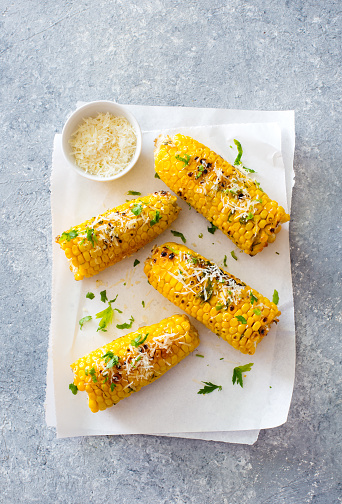 Ears of corn baked with herbs and parmesan cheese on white baking paper close up. Flat lat