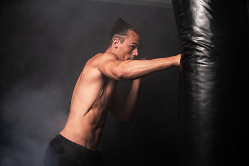Portrait of young male practicing boxing against black background. African Male boxer throwing a punch in front. Young sportsman training boxing.