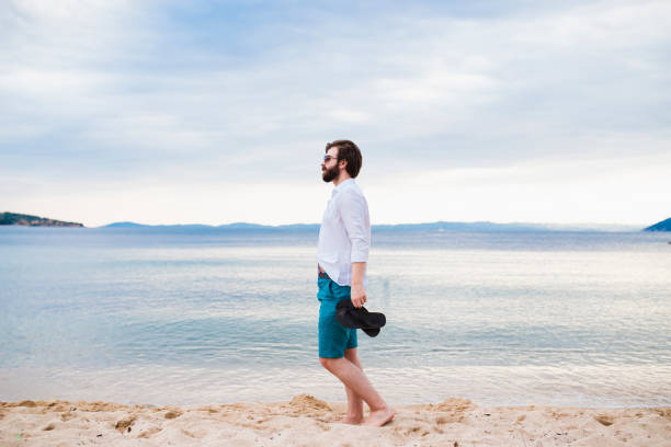 istock Young handsome man relaxing and walking at the beach 1263927587
