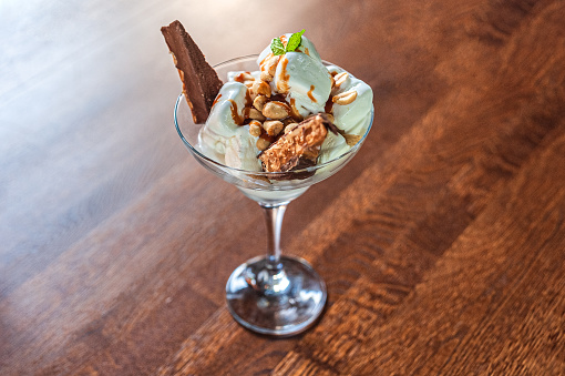 Dessert of white ice cream, peanuts and a chocolate bar with a mint leaf in a glass bowl on a wooden table