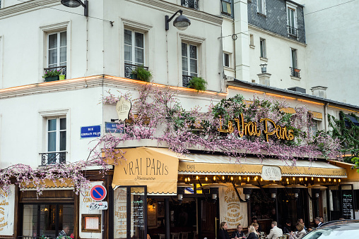 Montmartre, Paris, France.  May 9, 2019.  Street scene in the Montmartre district. Wisteria growing over the building, tourists or locals enjoying the outdoor seating.