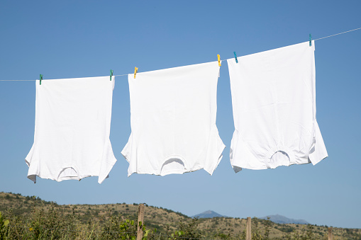White T-shirt hangs on a rope  in a sunny summer day with clear blue sky at the background