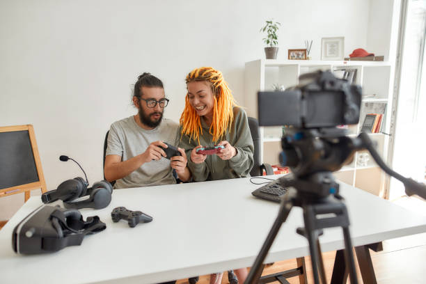 istock Man and woman using, discussing game controller joystick. Young male and female technology blogger recording video blog or vlog about new gadgets at home 1263938619