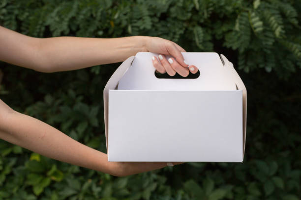 recevoir l’emballage de la maquette de cuisson. fermez les tenants femelles dans les mains dessert de gâteau dans la boîte vide vide non marquée en carton. zone publicitaire. recevoir le paquet de maquette. concept de livraison. - cake box packaging recycling photos et images de collection