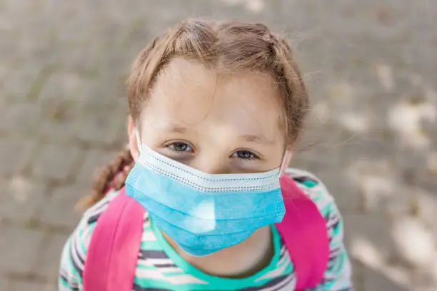 Close-up portrait of a school-age girl with a protective medical mask on her face. New school year in 2020. Protecting children during the coronavirus period in educational institutions.