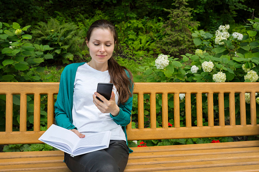 Outdoor portrait of a college student with a phone and a book.